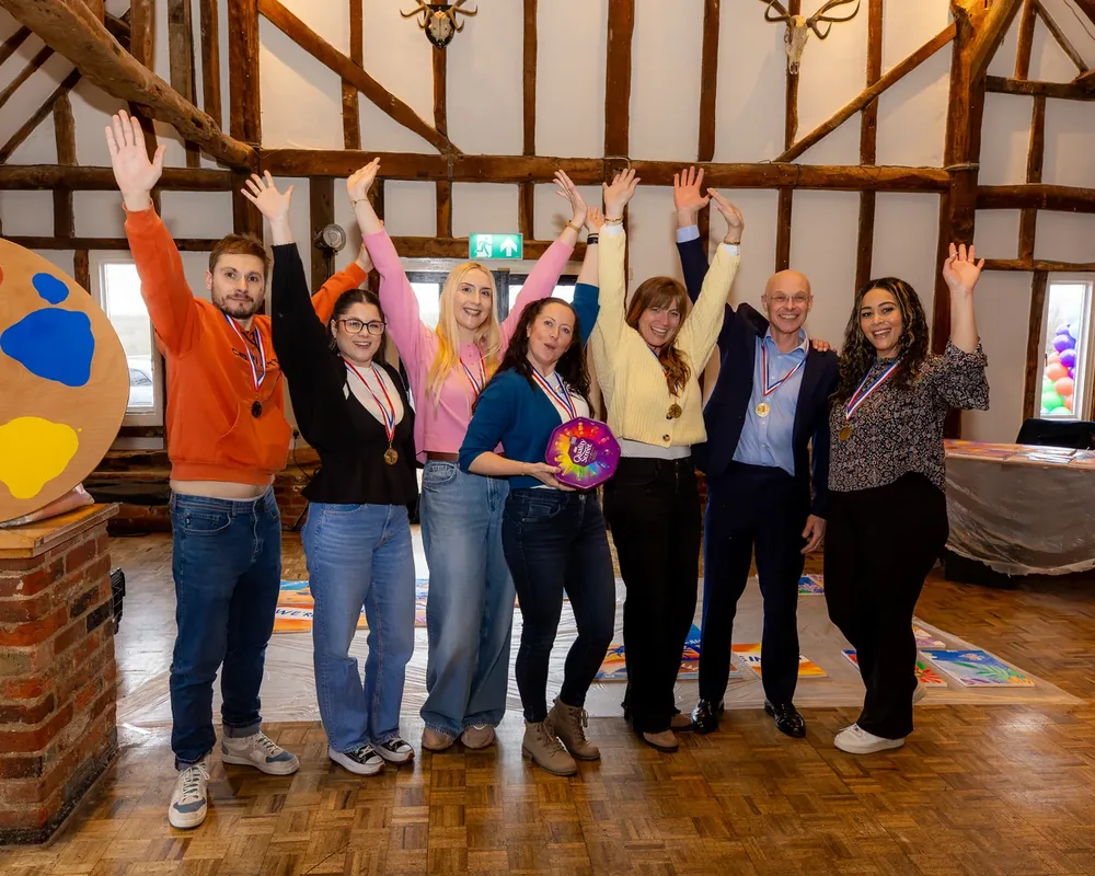 Eight members of the Innovative Trials team in a timber-beamed barn, arms raised and wearing medals