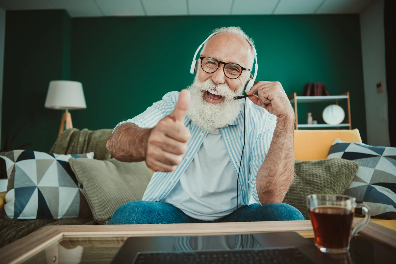 An older man at home on a headset, giving a thumbs up