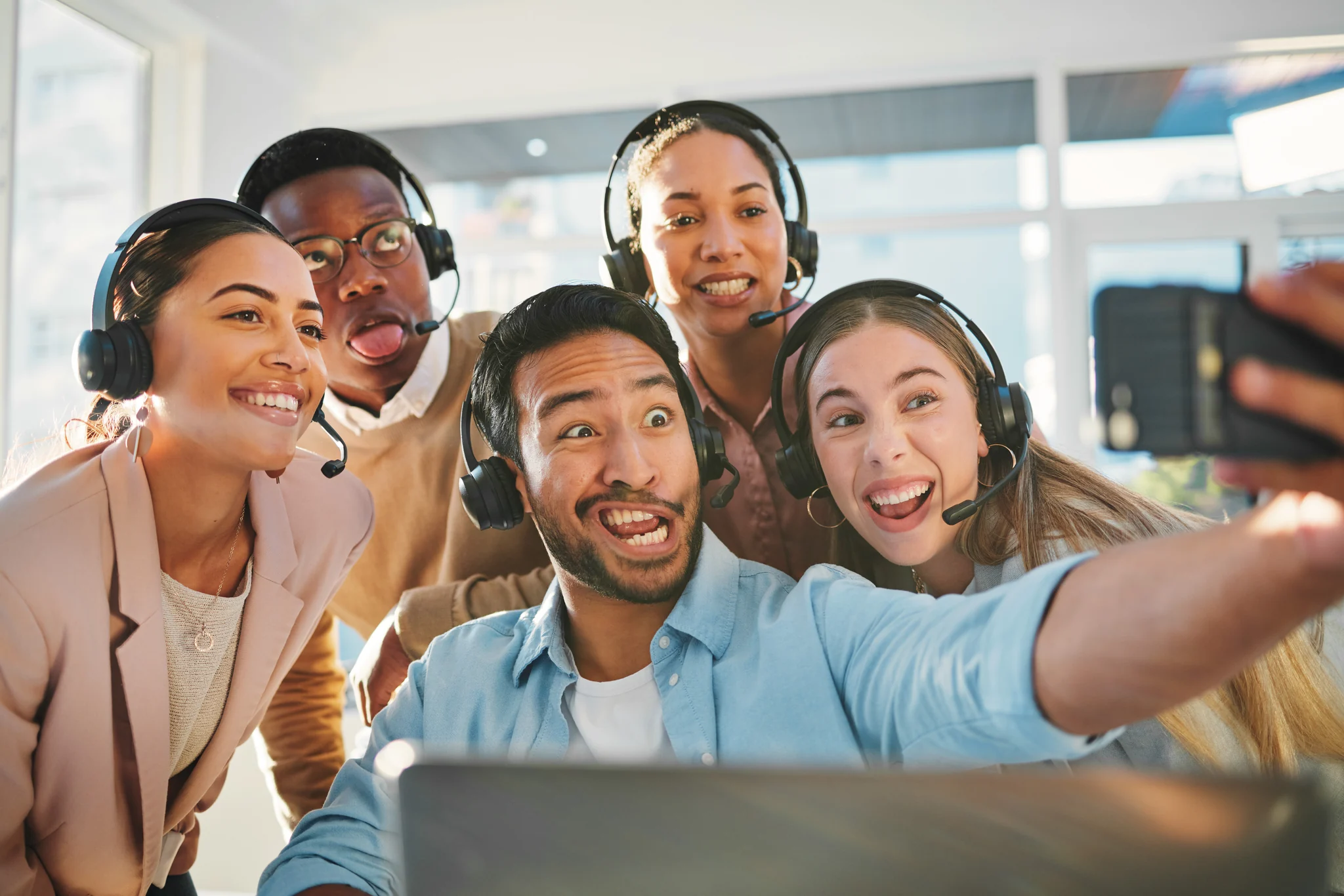 A support team in headsets crowded round a phone, laughing