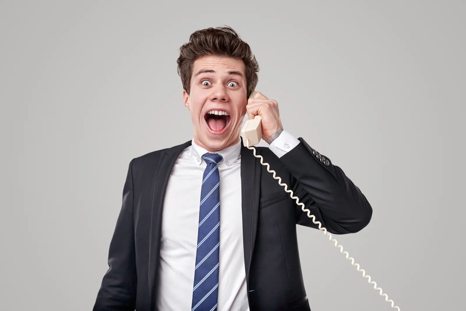 A young man in a suit shouting excitedly into a corded phone