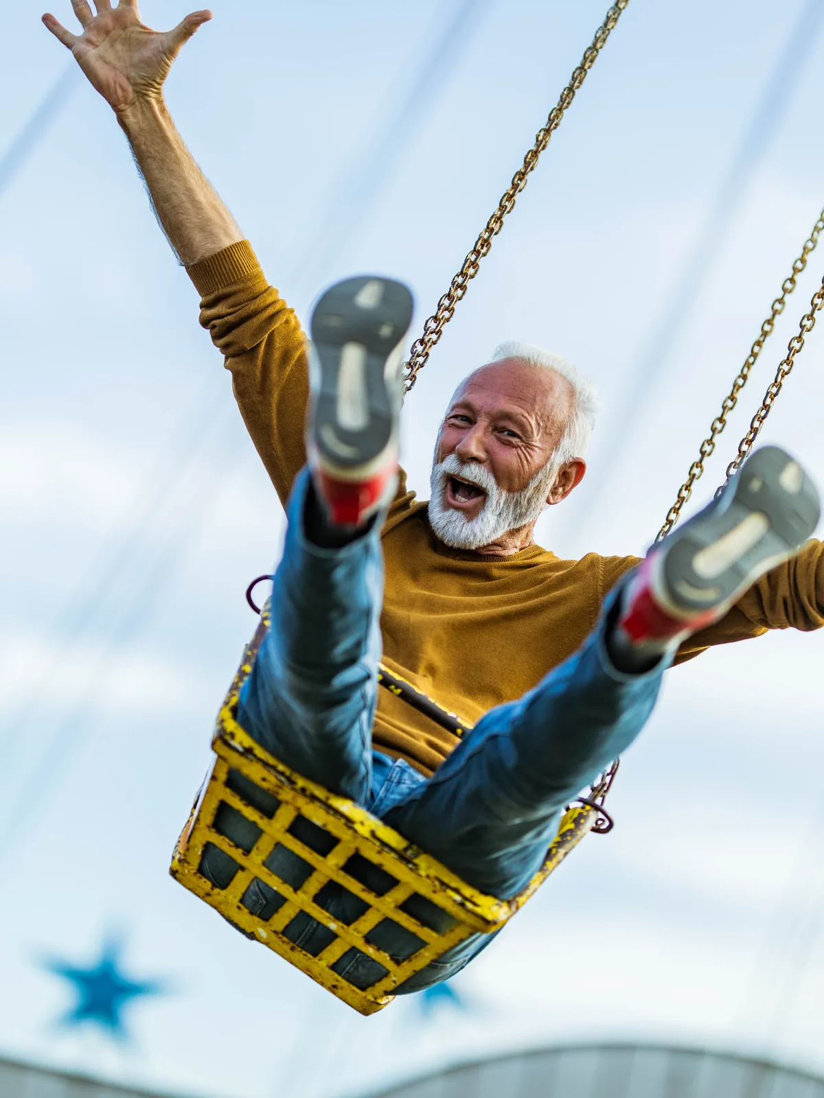 An older man on a swing, arms out, delighted