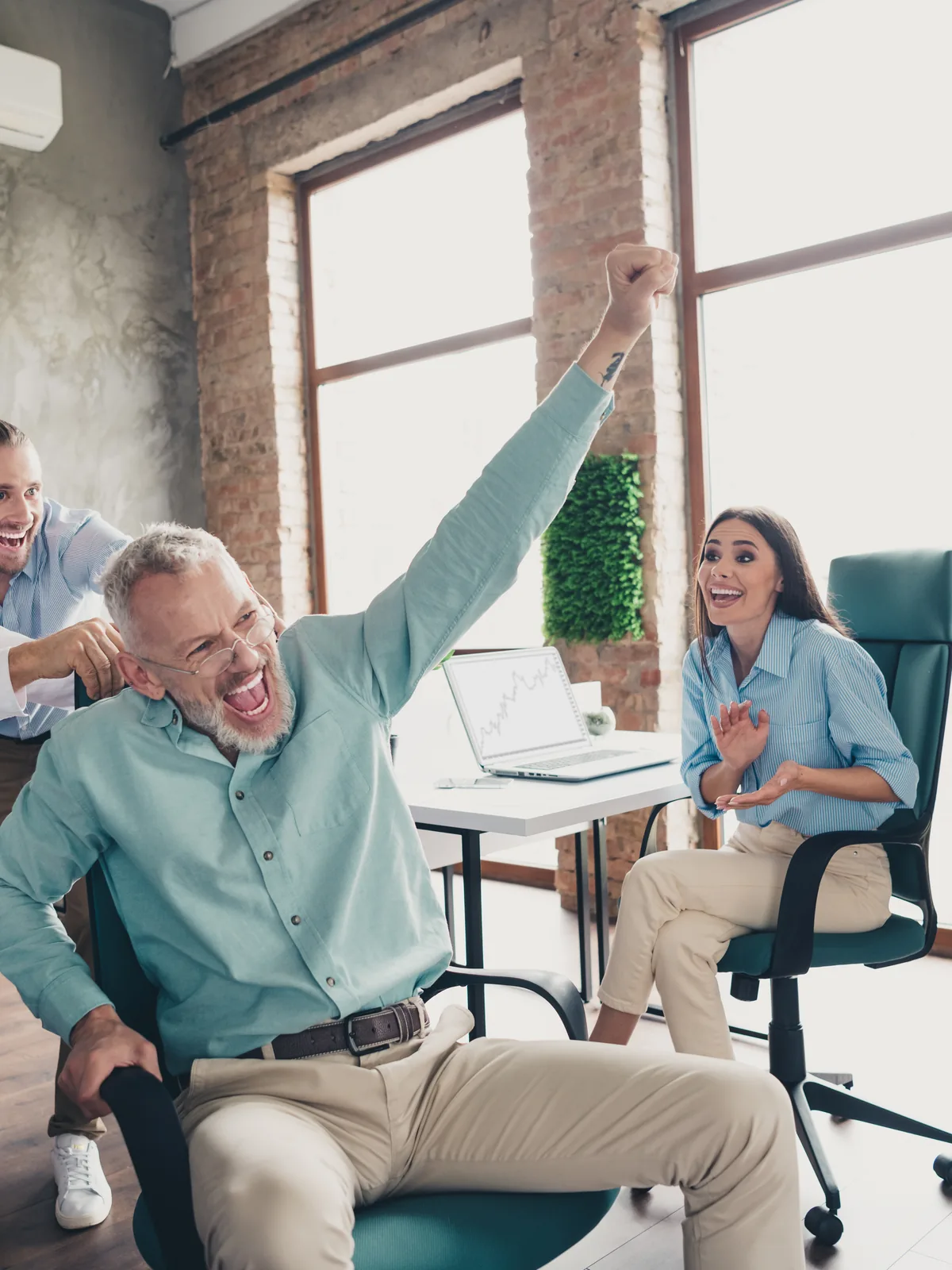 Colleagues cheering as one of them spins in his office chair, fist in the air