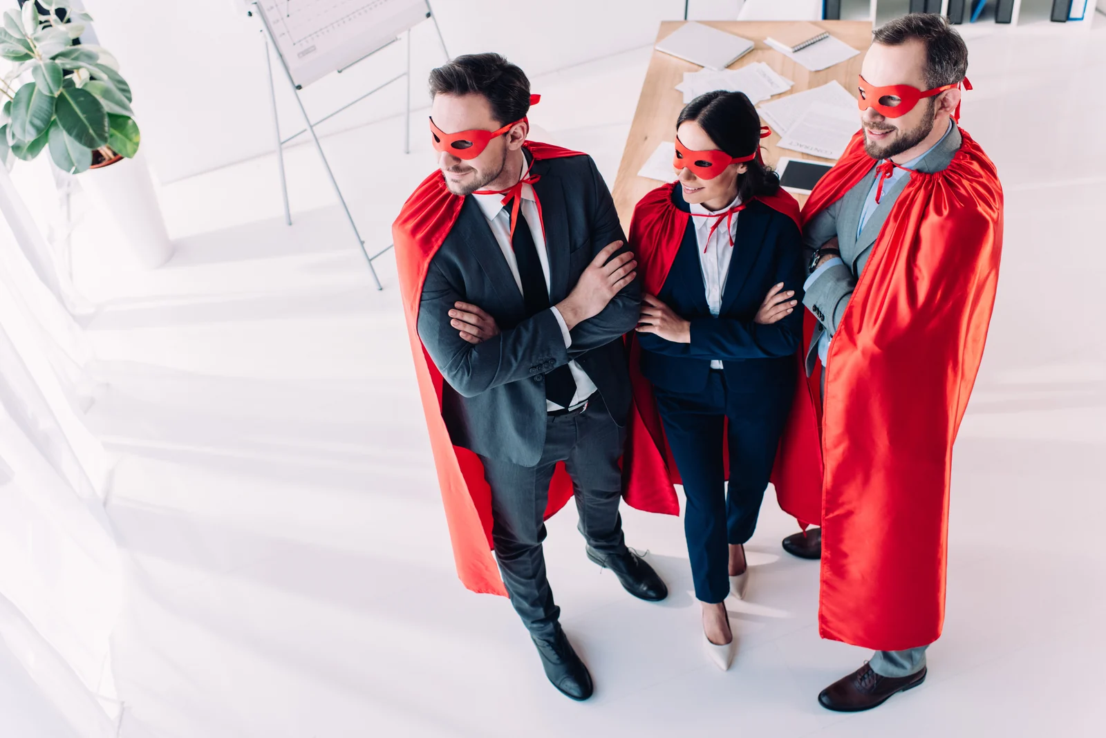 Three colleagues in superhero capes, arms folded