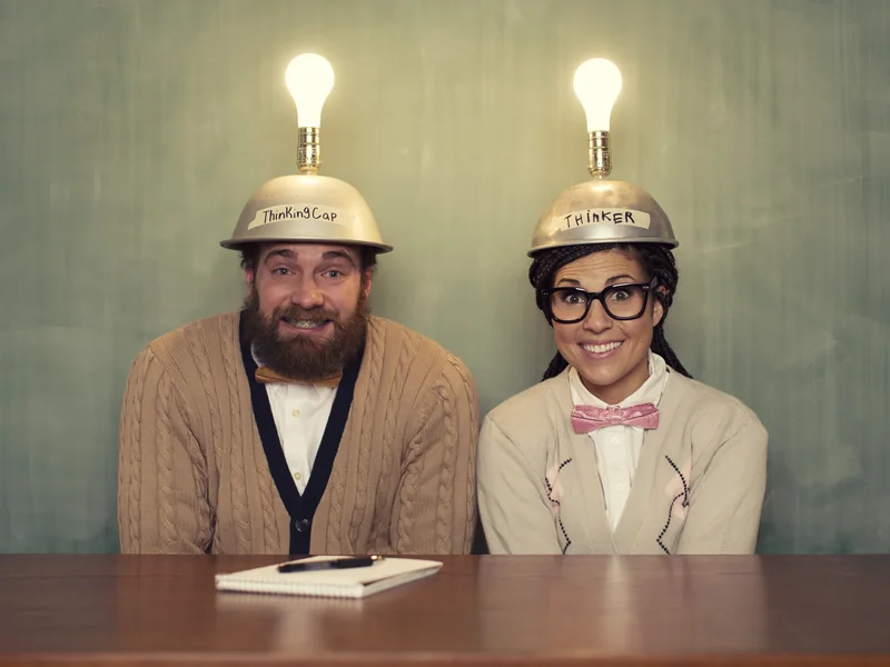 Two educators in lit-up lightbulb helmets, smiling behind a desk