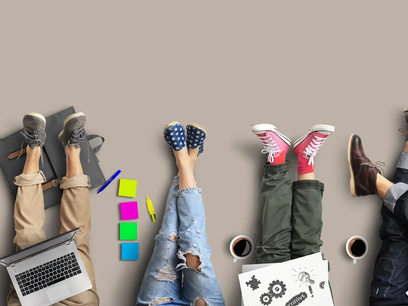 A row of people lying with their feet up the wall, among laptops, notes and coffee