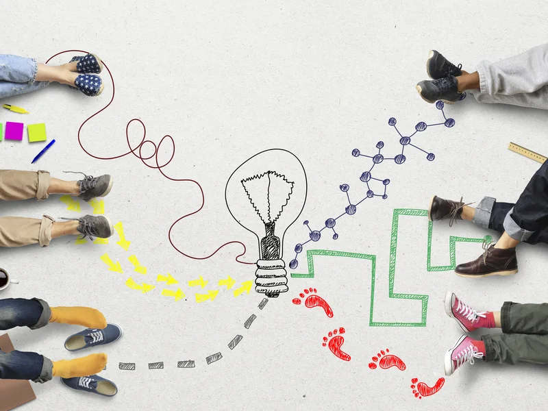 People sitting in a circle, their feet round a sketched lightbulb and the paths leading to it