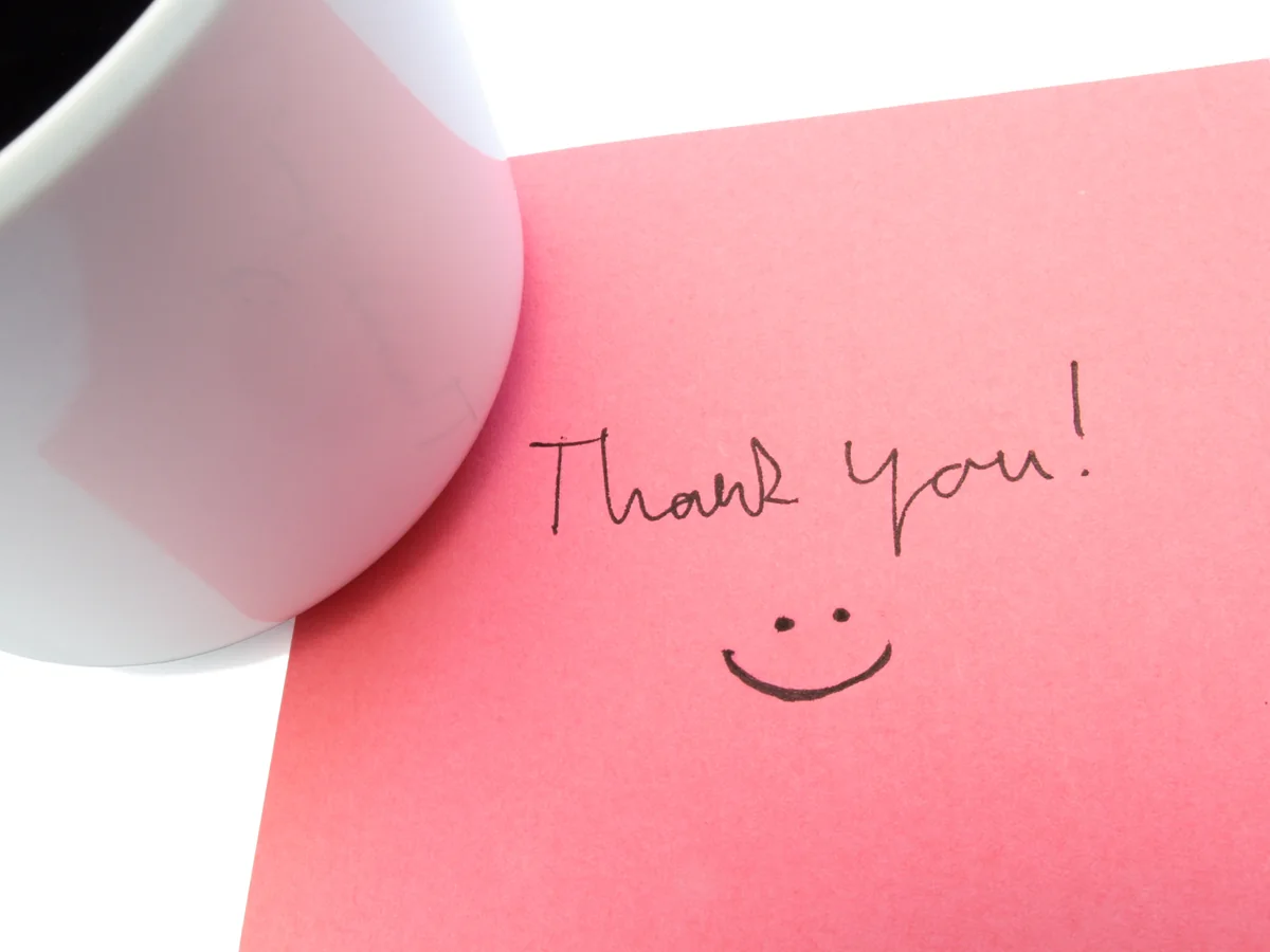 A pink card reading Thank you! with a smiley face, beside a white mug