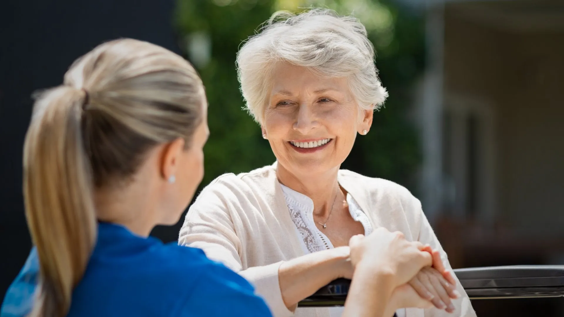 A nurse and an older woman talking outdoors, her hand resting on the nurse's arm